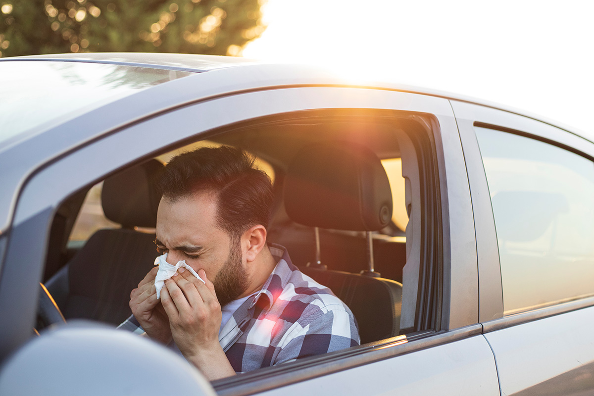 Man experiencing seasonal allergy symptoms outdoors in his car during fall